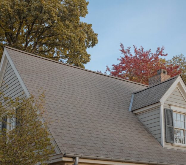A custom-built residential home with a high-quality light brown asphalt shingle roof, dormer window, and grey siding.