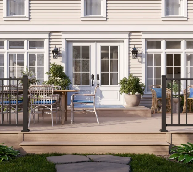 Elevated cottage-style composite deck with black aluminum balusters, light tan decking boards, and outdoor dining furniture in front of a white colonial home
