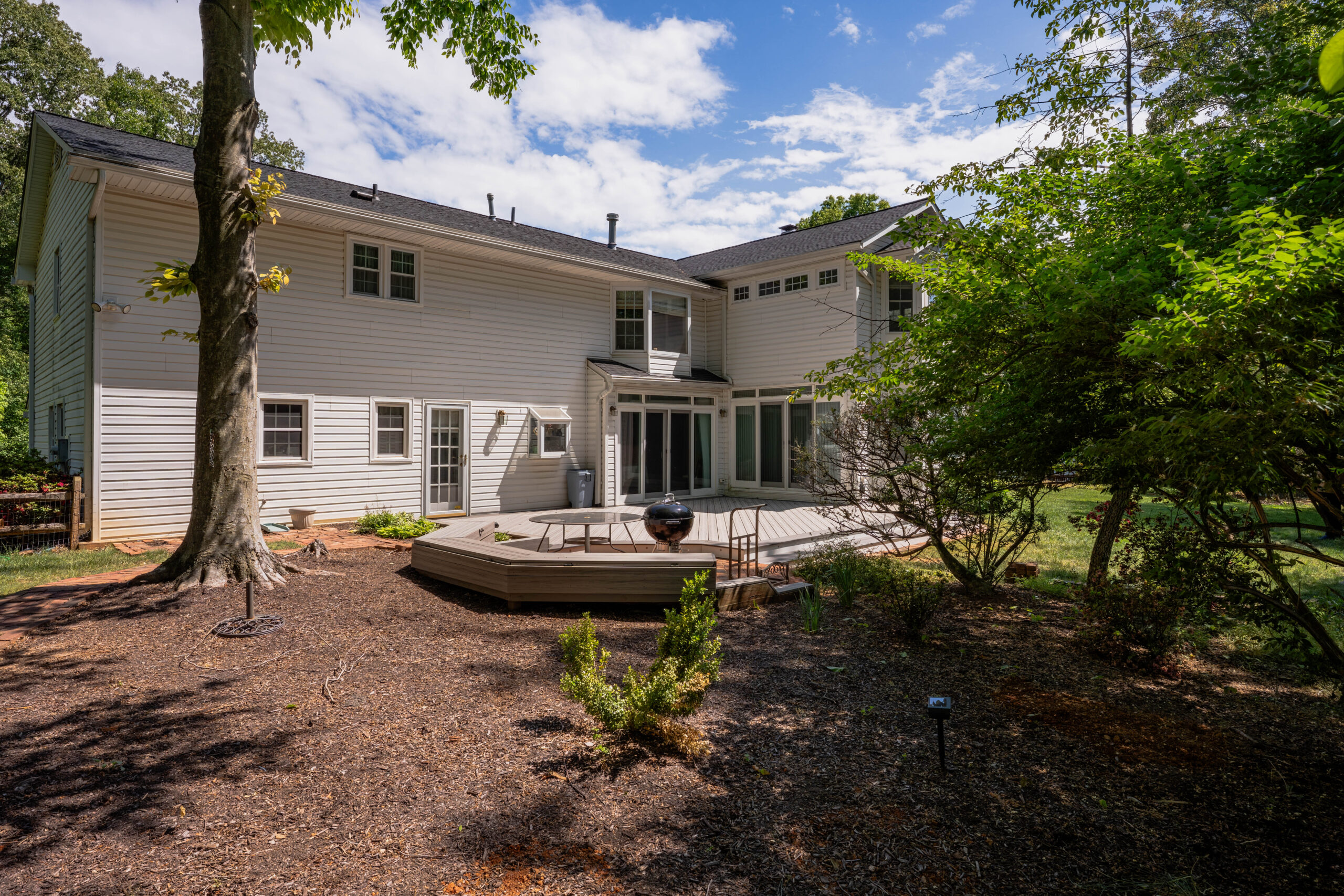 Composite deck and tiered bench seating set among mature trees in a wooded Vienna, VA backyard