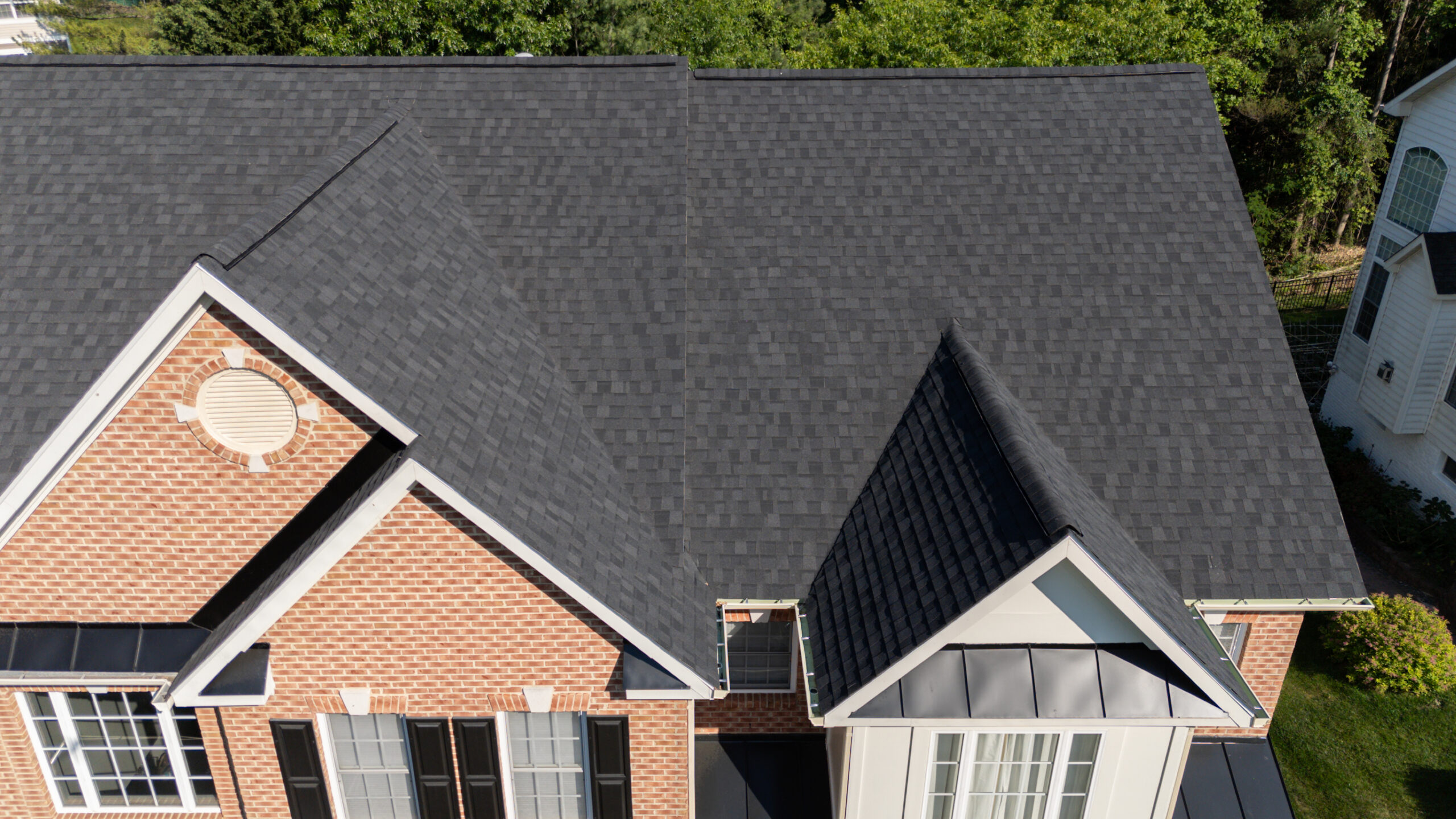 Aerial side view of Fairfax VA brick home showing new dark asphalt shingle main roof alongside black standing seam metal garage roof, by Noverra Exteriors